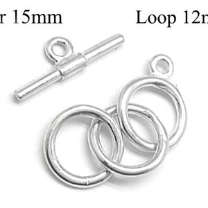 Könnte beinhalten: Silberner Toggle-Verschluss mit einer 15 mm Stange und einer 12 mm Schlaufe. Die Schlaufe besteht aus drei ineinandergreifenden Kreisen.