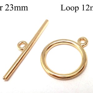 Könnte beinhalten: Goldfarbener Metall-Schiebeverschluss mit einem 23 mm langen Stab und einer 12 mm großen Schlaufe. Der Stab hat an einem Ende eine kleine Schlaufe. Die Schlaufe ist rund mit einer kleinen Schlaufe oben.