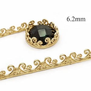 May include: A gold-colored jewelry component with a dark green gemstone, measuring 6.2mm. The component features an ornate, swirling design around the gemstone and along a separate decorative strip. The design is detailed and elegant.