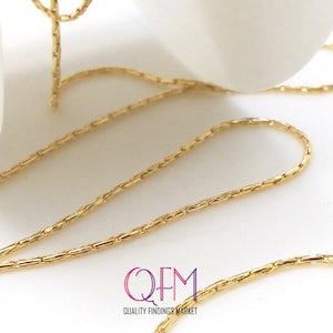 Könnte beinhalten: Nahaufnahme einer goldenen Kette mit einem Gliederkettenmuster. Die Kette liegt auf einer weißen Oberfläche. Der Text "QFM QUALITY FINDINGS MARKET" ist in der unteren rechten Ecke des Bildes sichtbar.