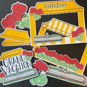May include: A colorful paper craft set featuring a Grand Hotel building, a striped awning, and a variety of flowers. The set includes the text "Grand Hotel Mackinac Island".