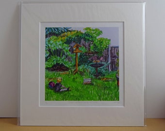 May include: A framed print of a garden scene with a person sitting on the grass. The artwork features a bird feeder, table, and lush greenery. The print is matted and encased in a clear protective sleeve.