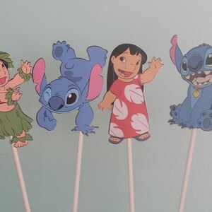 May include: Four cartoon character cutouts on sticks. The characters include Lilo in a red dress, Stitch in various poses, and a girl in a grass skirt. The characters are blue, red, green, and tan.