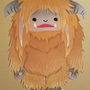 May include: A brown and yellow cartoon monster with a big smile and long hair. The monster has two small horns and is standing on a stick.