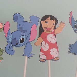 May include: Four cartoon character cutouts on sticks. The characters include a girl in a grass skirt, a blue alien, a girl in a red dress, and a blue alien. The characters are from the animated film Lilo & Stitch.