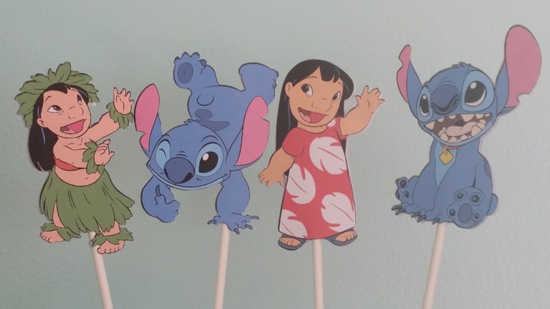 May include: Four cartoon character cutouts on sticks. The characters include a girl in a grass skirt, a blue alien, a girl in a red dress, and a blue alien. The characters are from the animated film Lilo & Stitch.