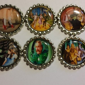 May include: Six silver bottle caps with images from the Wizard of Oz movie. The images include Dorothy's ruby slippers, the yellow brick road, the Wicked Witch of the West, the Wizard, and the Cowardly Lion.
