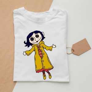 May include: White t-shirt with a cartoon illustration of a girl with blue hair wearing a yellow raincoat. The girl has large eyes and a red mouth.