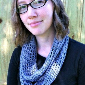 May include: A woman wearing a blue crocheted infinity scarf. The scarf is made with a simple stitch pattern and has a gradient of color from light blue to dark blue.
