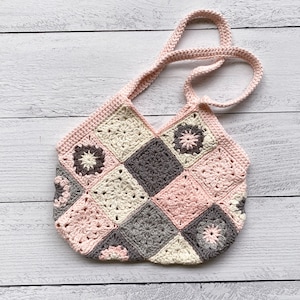 May include: A crocheted tote bag with a patchwork design featuring pink, cream, and gray squares. The bag has a single strap and is made with a granny square stitch.