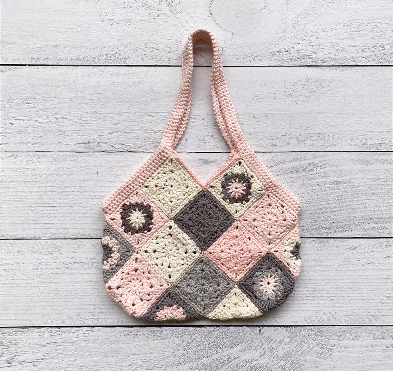 May include: A pink and gray crocheted tote bag with a square patchwork design. The bag has a single handle and is made with a variety of different stitches.