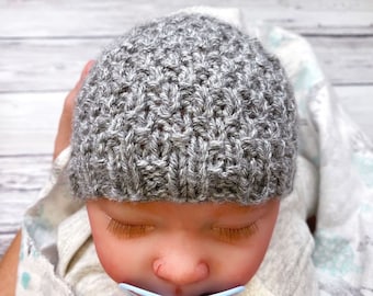May include: A gray knitted baby hat with a textured stitch pattern. The hat is on a baby doll with closed eyes.