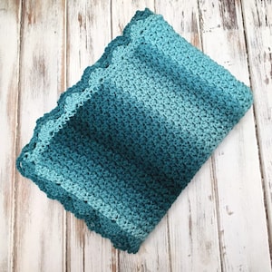 May include: A crocheted baby blanket in shades of teal and blue with a scalloped edge.