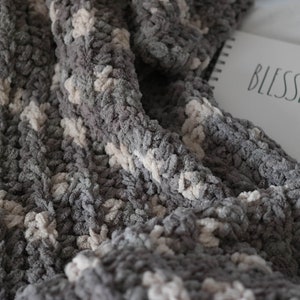 May include: A gray and cream chunky knit throw blanket with the word "BLESSED" written on a white notebook.