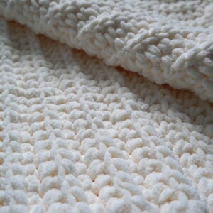 K&ouml;nnte beinhalten: Nahaufnahme einer cremefarbenen, grob gestrickten Decke. Der weiche, strukturierte Stoff ist gefaltet und zeigt die dicken, geschlungenen Maschen. Die Decke wirkt gem&uuml;tlich und warm, ideal f&uuml;r die Inneneinrichtung.
