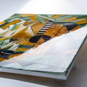 May include: A square canvas painting with a geometric abstract design in shades of yellow, green, black, and white. The painting has a glossy finish and is displayed on a white easel.