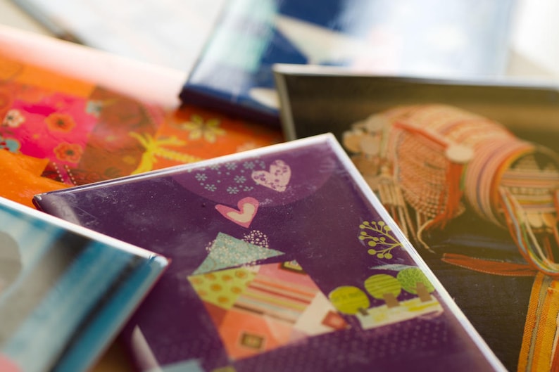 May include: A stack of colorful cards with different designs. The top card features a purple background with a white heart and a stylized house with a colorful roof. The card below it has a bright orange background with a floral design.