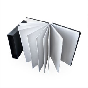 Op de afbeelding: Een zwart hardback schetsboek met witte pagina's, opengeklapt om de lege pagina's binnenin te laten zien.