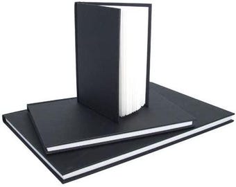 May include: Three black hardcover books with white-edged pages are stacked. One book stands upright, revealing its white interior pages. The other two books are lying flat, showcasing their black covers and white edges. The books are on a white background.