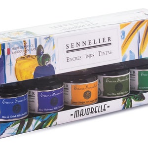 May include: A boxed set of Sennelier ink bottles. The packaging features the brand name and the text "ENCRES INKS TINTAS". The set includes five 30 ml ink bottles in various colors, including blue, orange, and green. The box has a decorative illustration.