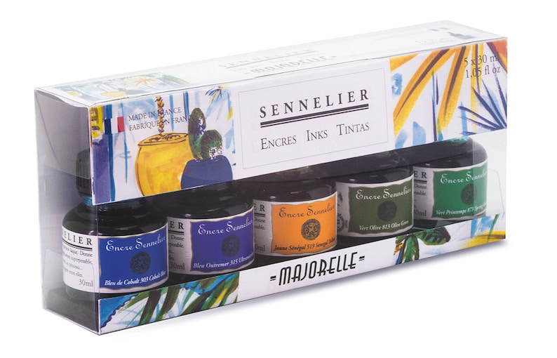 May include: A boxed set of Sennelier ink bottles. The packaging features the brand name and the text "ENCRES INKS TINTAS". The set includes five 30 ml ink bottles in various colors, including blue, orange, and green. The box has a decorative illustration.