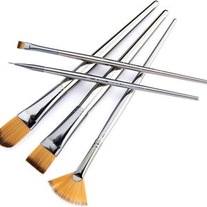 Puede incluir: Un conjunto de pinceles de artista con mangos plateados y cerdas color canela. Los pinceles están dispuestos en varios ángulos, mostrando diferentes formas de cabezales, incluyendo diseños planos, puntiagudos y en forma de abanico. Las cerdas son de color canela claro.