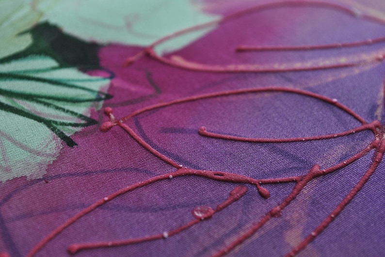 May include: Close-up of a purple fabric with a design of red lines and swirls. The fabric has a textured surface.