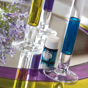 Pu&ograve; includere: Un piccolo flacone di vernice per vetri blu con un tappo bianco. Il flacone &egrave; appoggiato su un vassoio di vetro con tre tubi di vetro riempiti di liquido giallo, viola e blu.