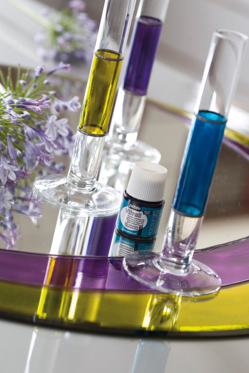 Pu&ograve; includere: Un piccolo flacone di vernice per vetri blu con un tappo bianco. Il flacone &egrave; appoggiato su un vassoio di vetro con tre tubi di vetro riempiti di liquido giallo, viola e blu.