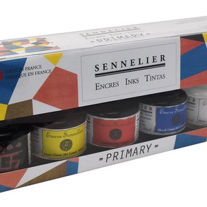 May include: A boxed set of Sennelier primary inks, made in France. The set includes five small glass jars of ink in various colors, including yellow, red, blue, black, and white. The packaging features the brand name and the text "PRIMARY".