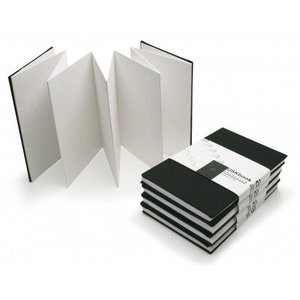 May include: A stack of black sketchbooks with the text "USKbook TRAVEL SKETCH" on the top book. The sketchbooks are closed and have a white spine.