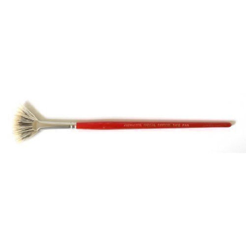 May include: A red handled fan brush with white bristles. The handle has the text "ARMSTRONG SPECIAL EFFECTS, TAIWAN" printed on it.