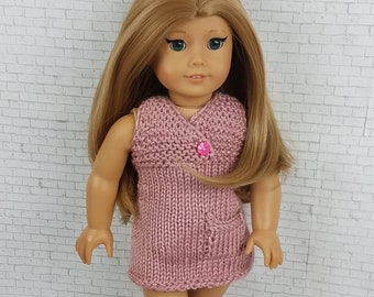 Könnte beinhalten: Ein rosa gestricktes Kleid mit einem einzigen Knopfverschluss und einer Tasche an der Seite, getragen von einer Puppe mit langen blonden Haaren und blauen Augen.