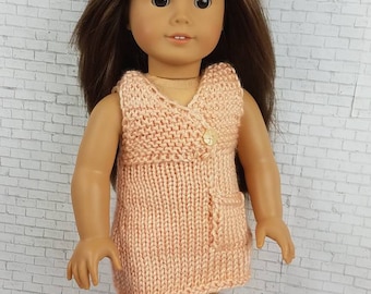 Könnte beinhalten: Ein peachfarbenes Strickkleid mit einem einzigen Knopfverschluss und einer Tasche an der Seite. Das Kleid ist für eine Puppe entworfen.
