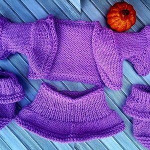 May include: A purple knitted baby outfit set including a cardigan, a skirt, and two pairs of booties.