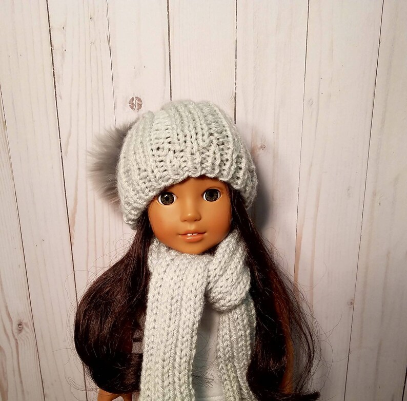 Puede incluir: Una mu&ntilde;eca con un gorro de punto gris con un pomp&oacute;n esponjoso y una bufanda a juego en gris.