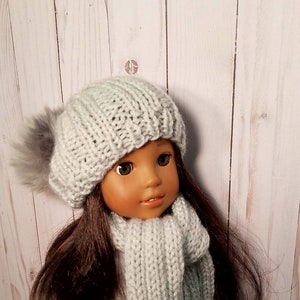 Puede incluir: Una mu&ntilde;eca con un gorro de punto gris con un pomp&oacute;n esponjoso y una bufanda a juego de color gris.