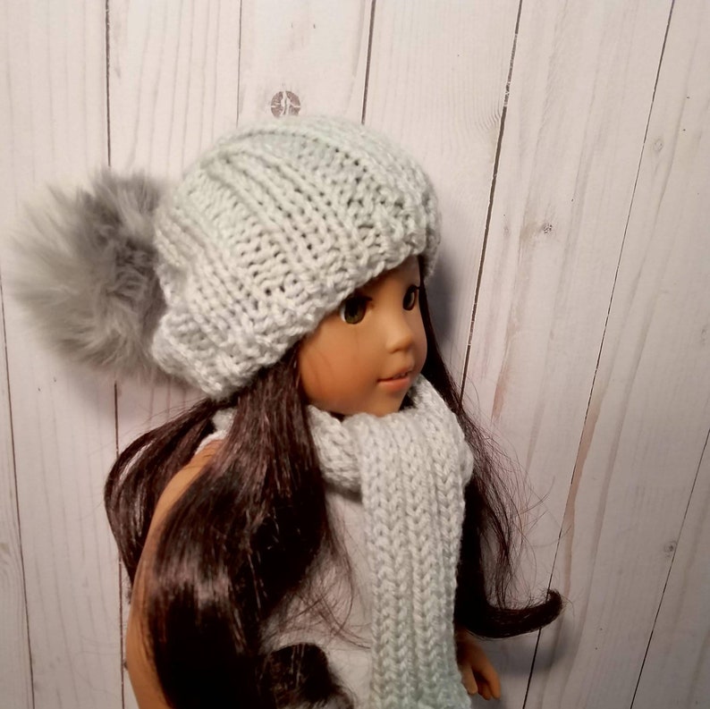 Puede incluir: Una mu&ntilde;eca con un gorro de punto gris con un pomp&oacute;n esponjoso y una bufanda gris a juego.