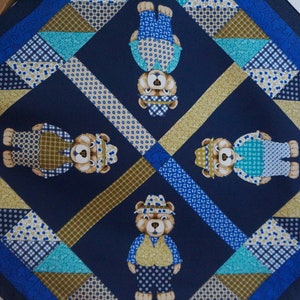 Può includere: Tessuto quadrato blu navy con un motivo ripetuto di orsetti in vari outfit. Il tessuto presenta disegni geometrici in blu, verde acqua e oro, creando un effetto patchwork. Gli orsi indossano cappelli e gilet.