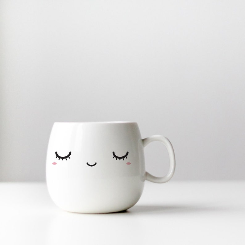 K&ouml;nnte beinhalten: Wei&szlig;e Keramiktasse mit einem niedlichen Comic-Gesicht mit geschlossenen Augen und einem L&auml;cheln.