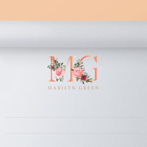 May include: A white sheet of paper with a rose gold monogram "MG" with floral accents. The text "MARILYN GREEN" is below the monogram.