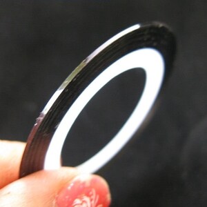 May include: A roll of black and white nail art tape. The tape is thin and has a metallic finish.