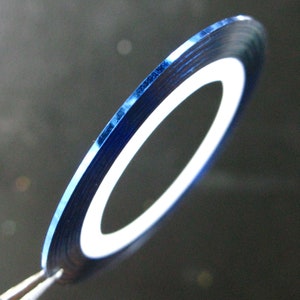 May include: A roll of blue metallic nail art tape with a white core. The tape is rolled into a circle and is being held by a pair of tweezers.