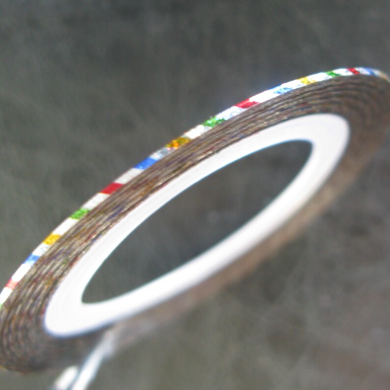May include: A roll of silver nail art tape with multi-colored stripes. The tape is on a white backing.