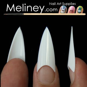 Puede incluir: Tres puntas de u&ntilde;as blancas en forma de estilete se muestran sobre un fondo negro. Las puntas son sostenidas por dedos, mostrando su dise&ntilde;o afilado y puntiagudo. La imagen incluye el texto "Meliney.com Nail Art Supplies".