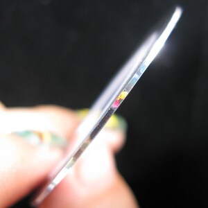 May include: Close-up of the edge of a clear, round disc with a rainbow-colored iridescent sheen.