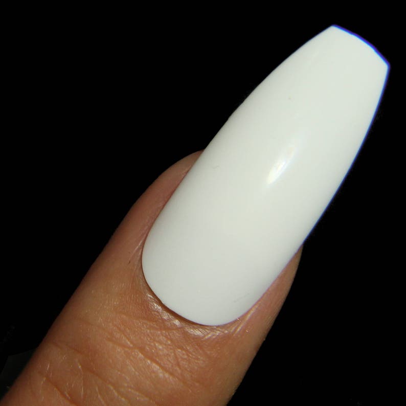 May include: A close-up of a white, long, oval-shaped artificial nail on a finger.