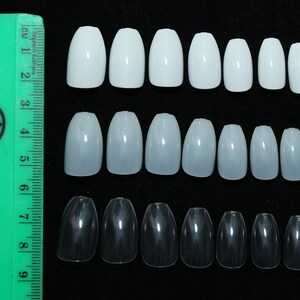 May include: Three rows of coffin-shaped false nails in white, light pink, and clear. The nails are arranged in size order from smallest to largest.
