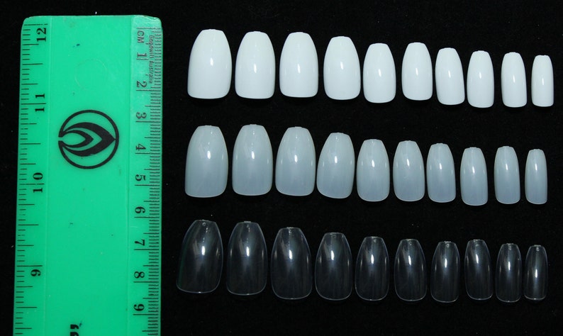 May include: Three rows of coffin-shaped false nails in white, light pink, and clear. The nails are arranged in size order from smallest to largest.