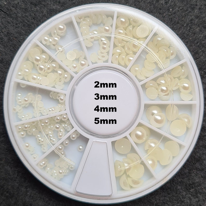 Pode incluir: Uma roda de pl&aacute;stico branca com 12 compartimentos contendo diferentes tamanhos de contas brancas peroladas. A roda &eacute; etiquetada com os tamanhos das contas: 2 mm, 3 mm, 4 mm e 5 mm.